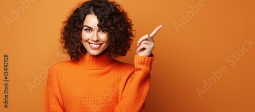 Young Caucasian brunette girl pointing to empty advertising space on orange background photo