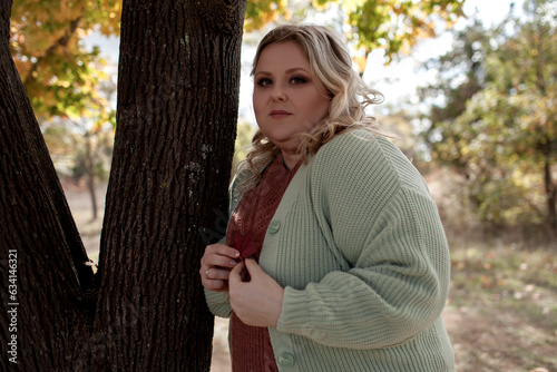 Beautiful plus size model walking in the fall park against yellow leaves/ Woman wearing warm fashion outfit. Overweight girl