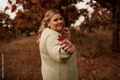 Beautiful plus size model walking in the fall park against yellow leaves  Woman wearing warm fashion outfit. Overweight girl