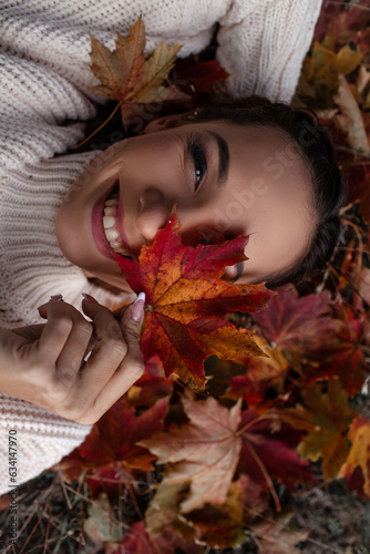 Portrait of a beautiful woman  hold the fall leaves and resting in the park. The happy girl wearing knitted sweate