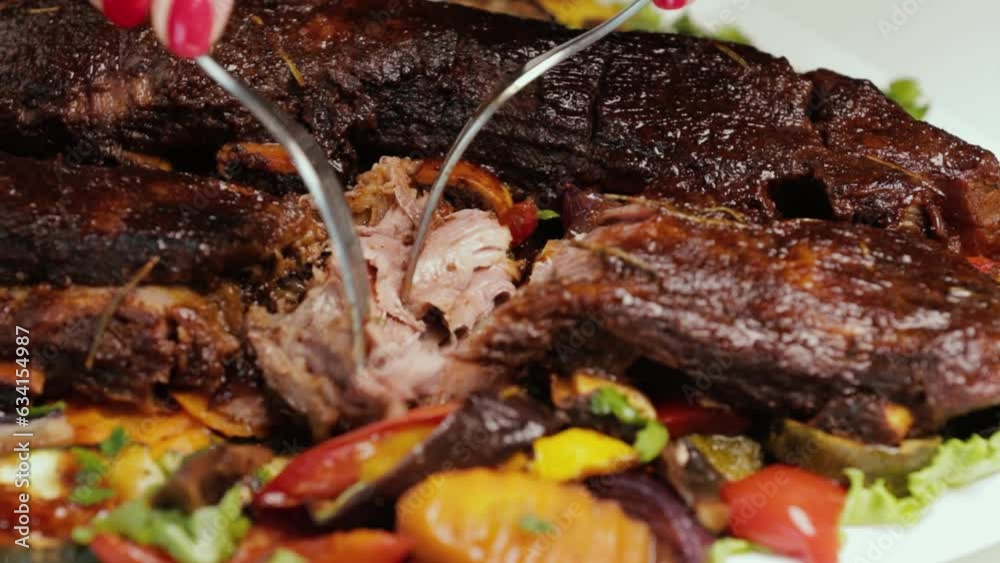 Grilled beef ribs and vegetables on a white plate. The chef shows how tender and juicy the meat turned out. Close-up on a black background Grilled beef ribs and vegetables on a white plate. The chef shows how tender and juicy the meat turned out. Close-up on a black background