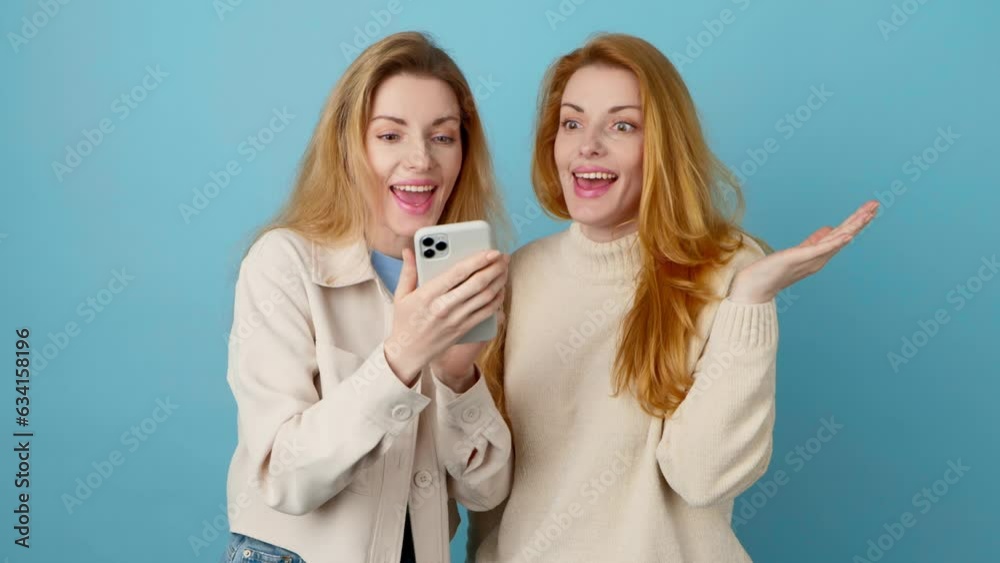 Mobile cell phone, friends say Wow and woman celebration for winning, discount or sale on blue background. Two women sister excited with smartphone for social media, online streaming, news or internet Mobile cell phone, friends say Wow and woman celebration for winning, discount or sale on blue background. Two women sister excited with smartphone for social media, online streaming, news or internet