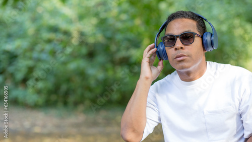 Relaxation in mountains. Young Hispanic with headphones sitting and listening to music