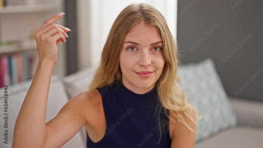 Young blonde woman sitting on sofa doing closing mouth gesture at home Young blonde woman sitting on sofa doing closing mouth gesture at home