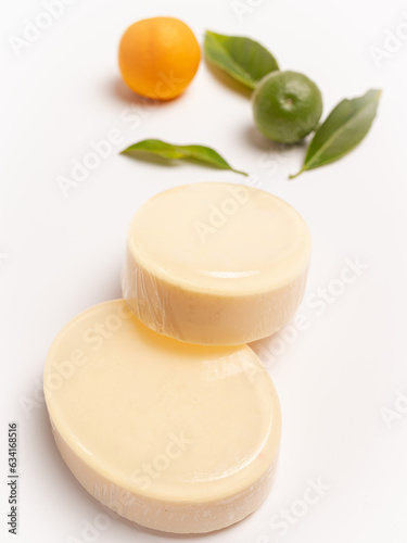 jabones artesanales cremosos en fondo blanco con hojas de limones y naranjas verdes y amarillas  