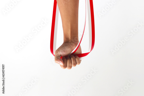 A man with a fist holding a red and white ribbon with empty copy space isolated on a white background, representing Indonesia Independence Day concept