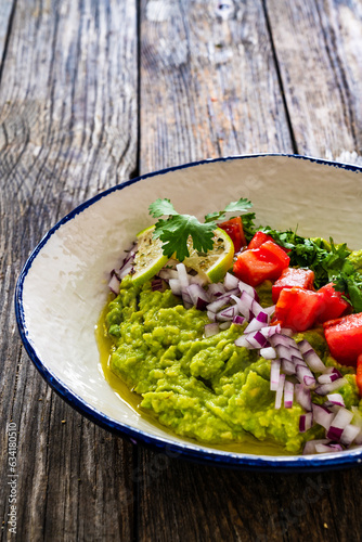 Guacamole with tomato, red onion and parsley on wooden table