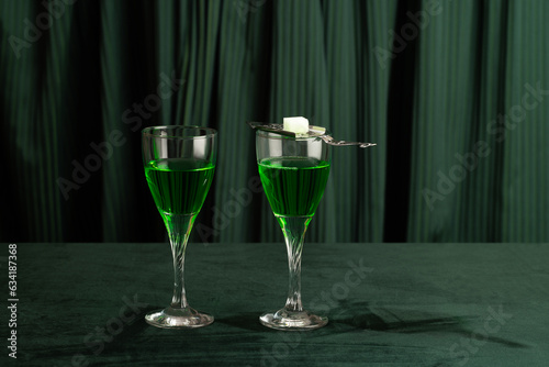 Two glasses of absinthe with a silver spoon and a cube of sugar on a green background photo