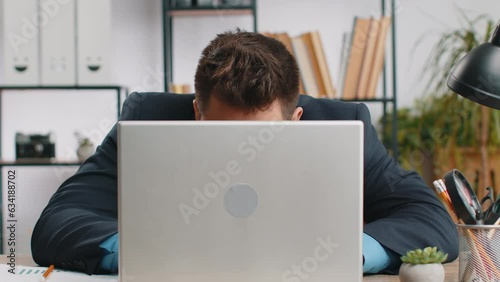 Confident young businessman hiding behind laptop computer, looking at camera, spying his colleagues working, peeping. Professional freelancer man looking from behind computer with cunning eyes glance