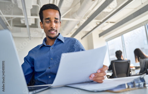 Busy young African American business man bank account manager sitting at office work checking documents. Ethnic businessman worker reading marketing plan or financial report at workplace.