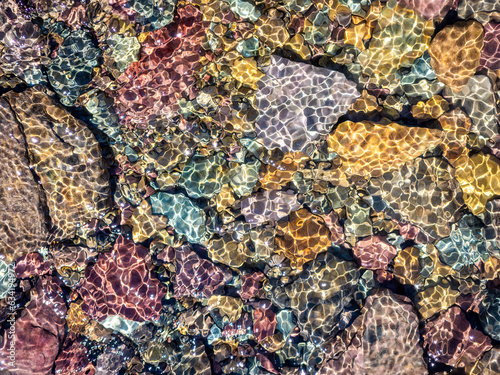 Close-up of multi-colored rocks in a creek near Logan Pass in Glacier National Park, Montana, USA. The flowing water sparks shiny specular highlights. photo