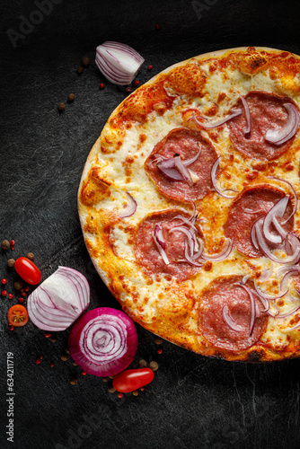 Pizza with salami sausage and red onion on a black background, top view