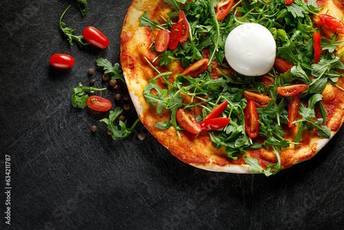 Pizza with cherry tomatoes, arugula and burrata cheese on a black background, top view