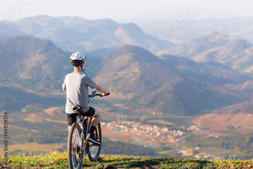 Obraz na plátně Cyclist resting with his mountain bike while admiring the mountainous landscape in the background