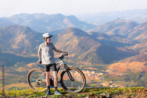 A Brazilian man standing still, taking a break with his mountain bike after cycling. He is at the top of a mountain