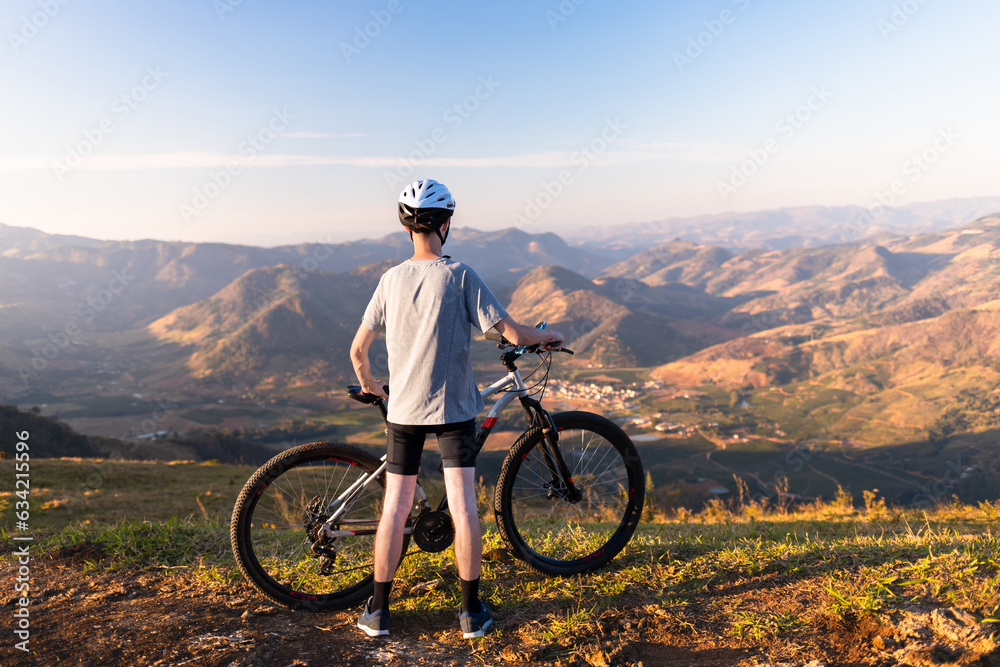 Fototapeta premium Cyclist resting with his mountain bike while admiring the mountainous landscape in the background.
