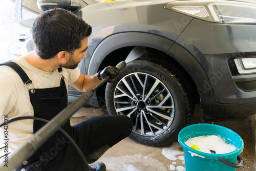 Professional hispanic worker pressure washing car undercarriage