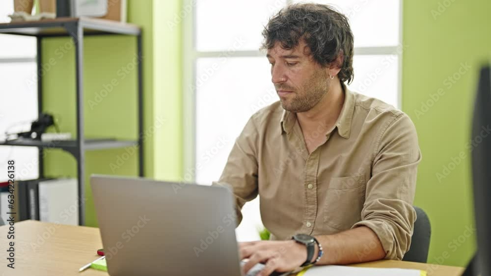 Young hispanic man business worker using laptop with serious face at office