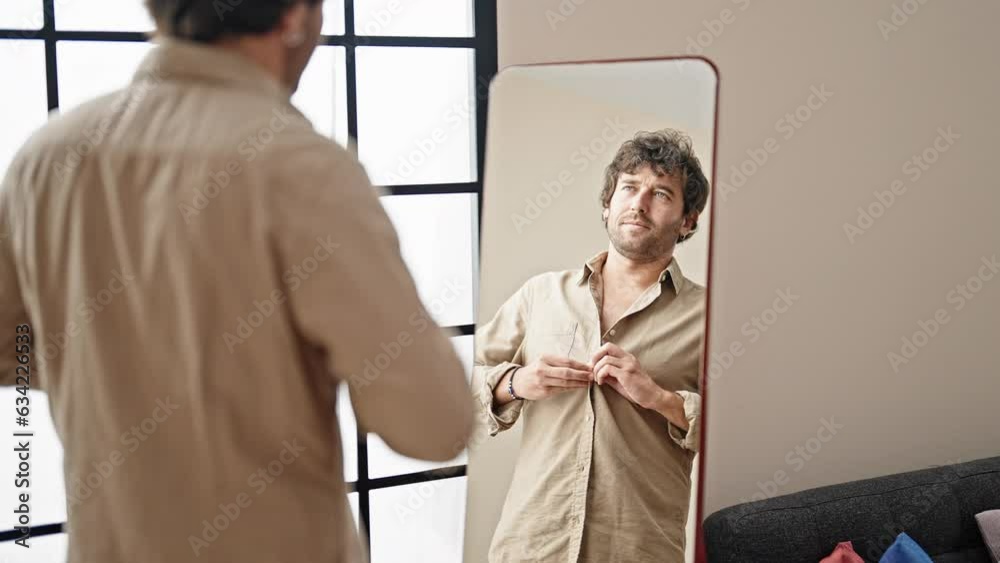 Young hispanic man wearing shirt looking on mirror at home Young hispanic man wearing shirt looking on mirror at home