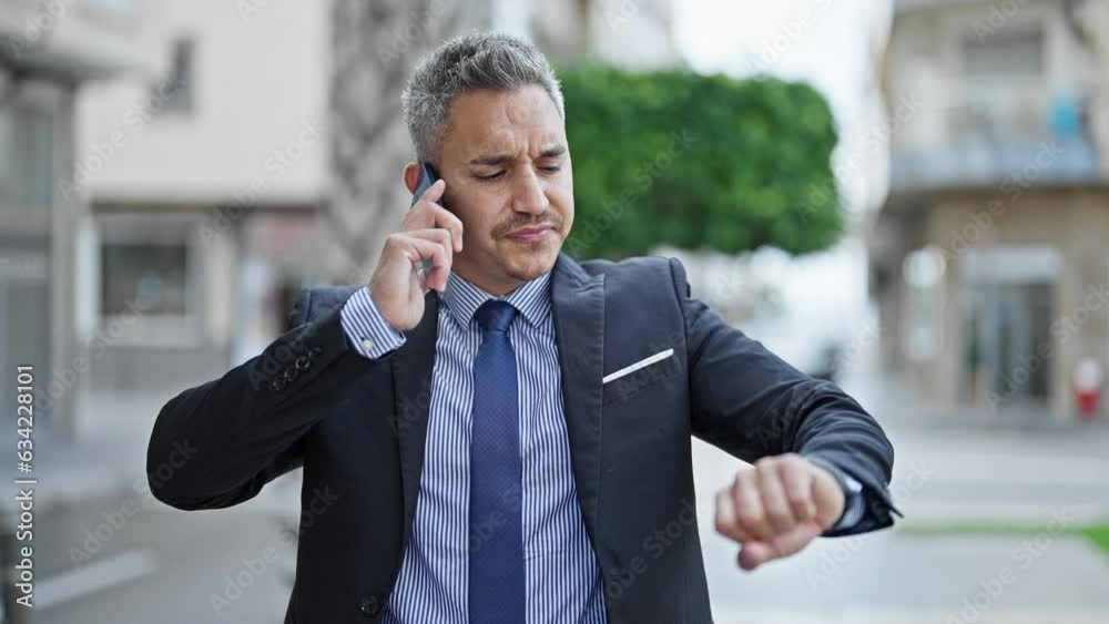 Young hispanic man business worker talking on smartphone looking watch at street Young hispanic man business worker talking on smartphone looking watch at street