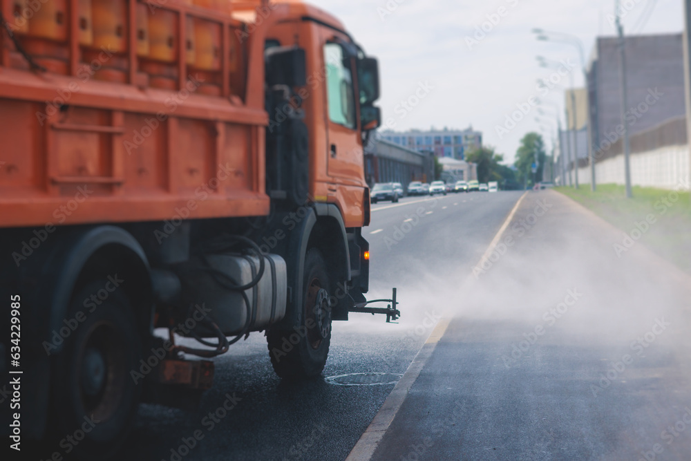 Municipal watering truck machines washes asphalt, process of street disinfection and cleaning from dust and dirt, cleaning flusher sweeper machines wash the city streets road with water spray