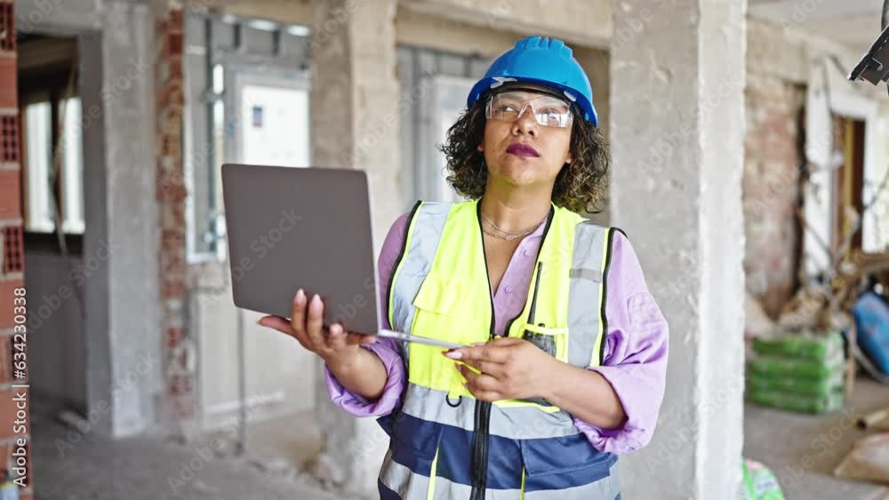 Young beautiful latin woman builder using laptop talking by walkie talkie at construction site Young beautiful latin woman builder using laptop talking by walkie talkie at construction site
