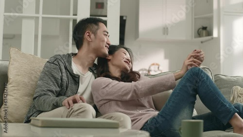 happy young asian couple sitting chatting on family couch at home photo