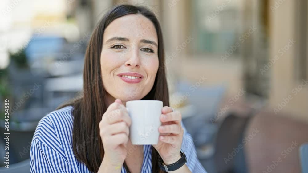 Young beautiful hispanic woman drinking coffee sitting on table at coffee shop terrace Young beautiful hispanic woman drinking coffee sitting on table at coffee shop terrace