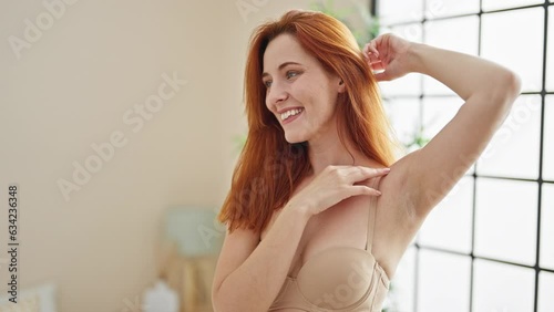 Young redhead woman wearing lingerie touching depilated armpit at bedroom photo