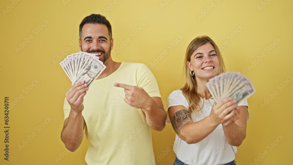 Man and woman couple smiling confident pointing to dollars over isolated yellow background Man and woman couple smiling confident pointing to dollars over isolated yellow background