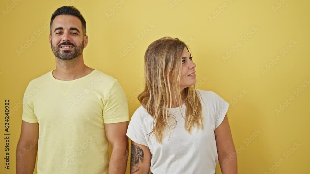 Man and woman couple standing together looking to the side surprised over isolated yellow background Man and woman couple standing together looking to the side surprised over isolated yellow background