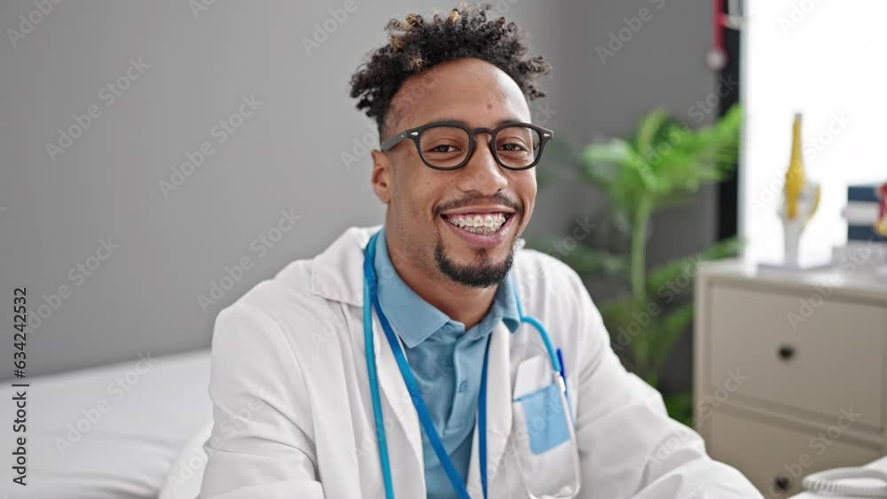 African american man doctor smiling confident sitting on table at clinic African american man doctor smiling confident sitting on table at clinic