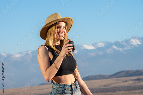 blonde girl drinking mate in the mountainous landscape of mendoza