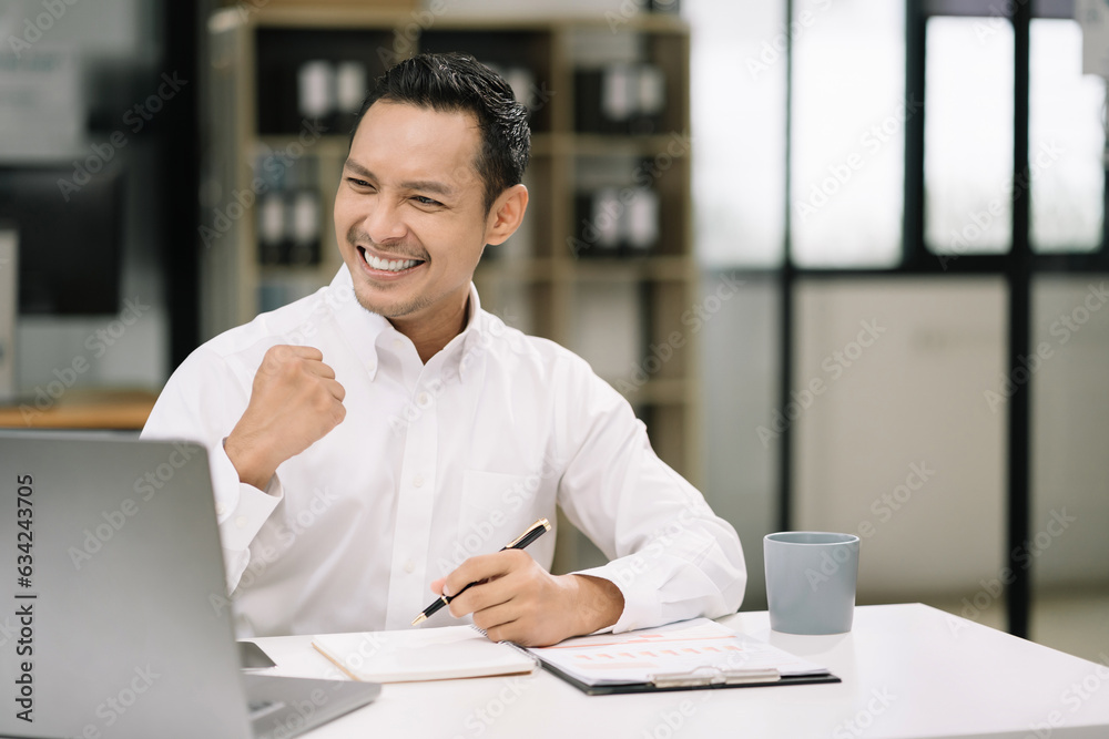 Fototapeta premium Successful business man, excited young man Keeping up arms and showing positive emotions, happy working in modern office on computer.