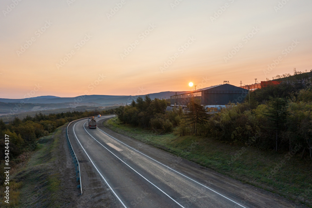 Morning aerial photograph of a highway. Sunrise over asphalt road and industrial buildings. The truck is driving along the road. Kolyma highway, Magadan region, Far East of Russia.