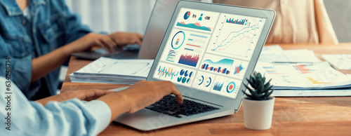 Panorama shot analyst team utilizing BI Fintech to analyze financial report with laptop. Businesspeople analyzing BI power dashboard displayed on laptop screen for business insight. Scrutinize