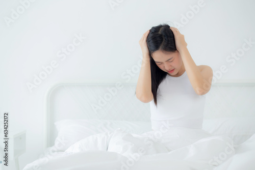 Young asian woman sitting on bed pain headache in the bedroom at home, unhappy female exhaustion and sick headache, anxiety and unwell, dizziness and disorder, medical and health concept.