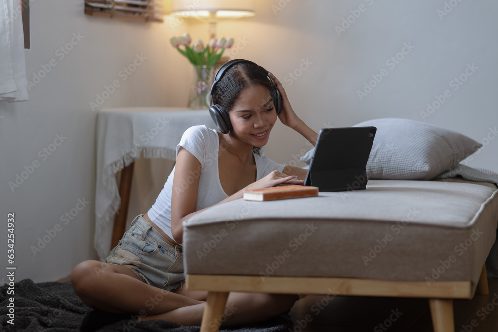 Young African woman holding tablet with earphones sitting on sofa at home.