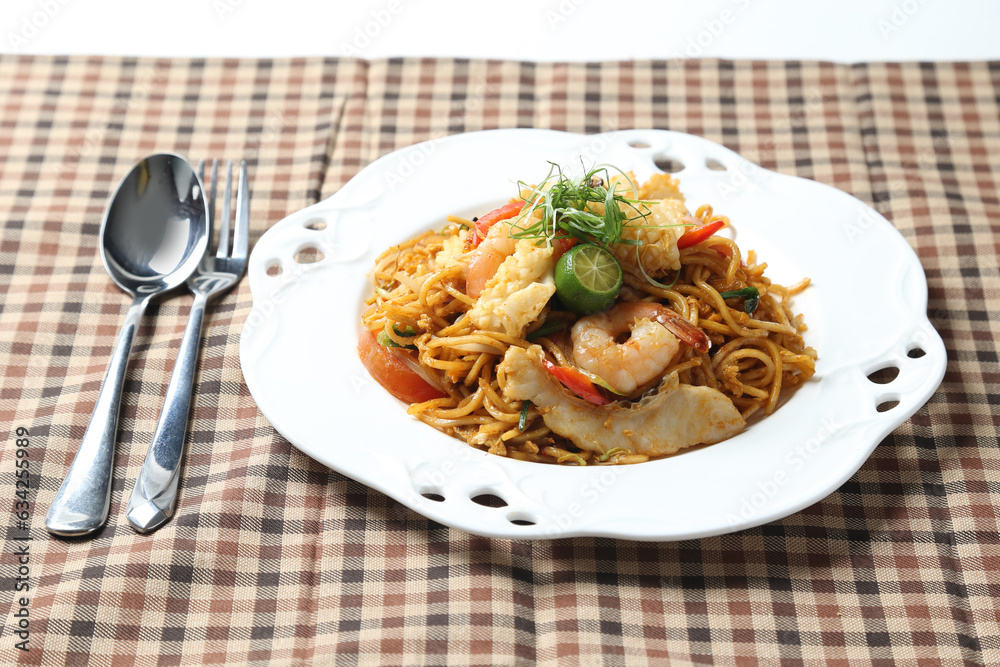stir fried Malay spicy chilli noodle mamak mee goreng with mixed seafood fish, prawn, squid, meat and lime in plate on white background asian chef cuisine halal food menu for cafe