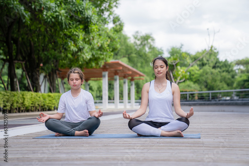 A happy girl exercising training in yoga and looking at the female instructor next to her in the park