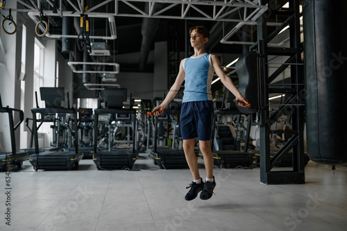 Sportive teenage boy skipping rope while training at gym