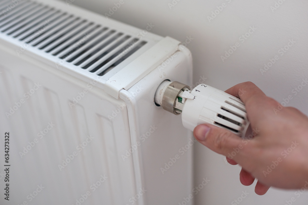Hand adjusting thermostat valve of heating radiator in a room. Hand adjusting thermostat valve of heating radiator in a room.