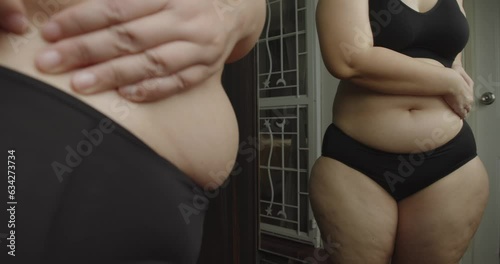 Asian oversize woman in front of a mirror looks at her body. Excess belly fat, Unhealthy lifestyle, Diet concept.