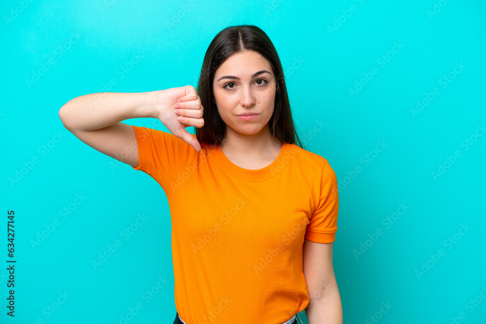 Young caucasian woman isolated on blue background showing thumb down with negative expression Young caucasian woman isolated on blue background showing thumb down with negative expression