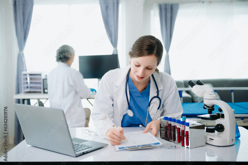 Confident young Caucasian female doctor in white medical uniform sit at desk working on computer. Smiling use laptop write in medical journal Confident young Caucasian female doctor in white medical uniform sit at desk working on computer. Smiling use laptop write in medical journal
