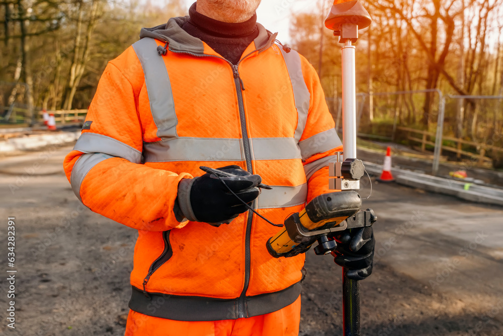 Site engineer operating his touch screen controller instrument during roadworks. Builder using