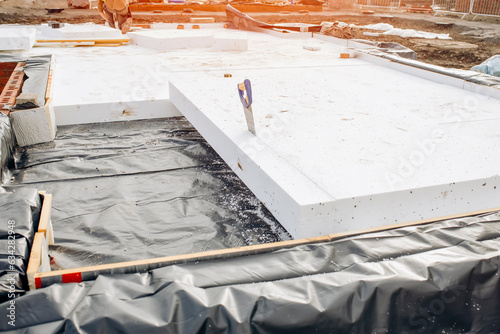 Builder placing polystyrene insulation boards on waterproofing membrane during floor construction. Energy saving concept photo