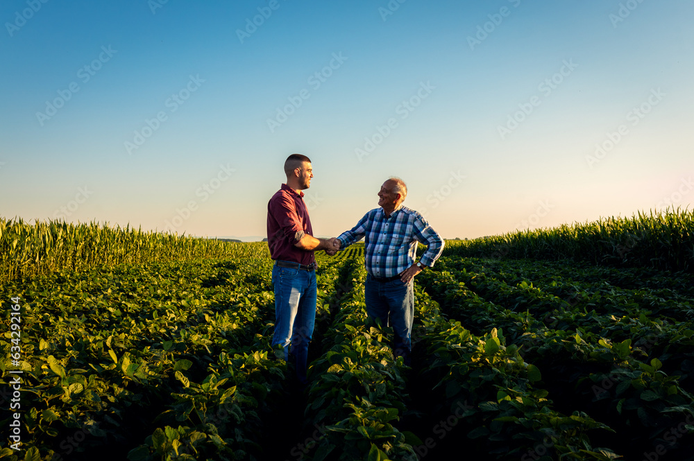 Two farmers in soy field making agreement with handshake at sunset.