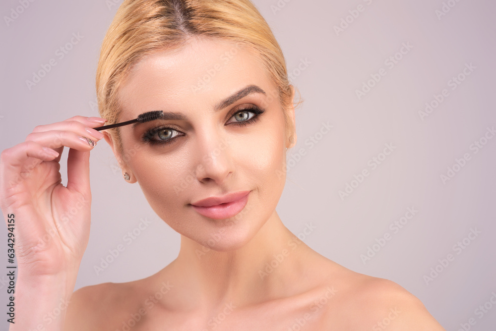 Beautiful woman applies brow gel with brows brush to her eyebrow. Studio portrait of young woman doing her eyebrow natural make up. Eyebrows make up concept.