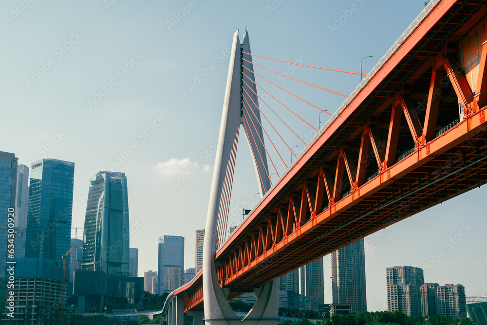 Low angle view of suspension bridge against sky with skycrapers and a river in the background Low angle view of suspension bridge against sky with skycrapers and a river in the background